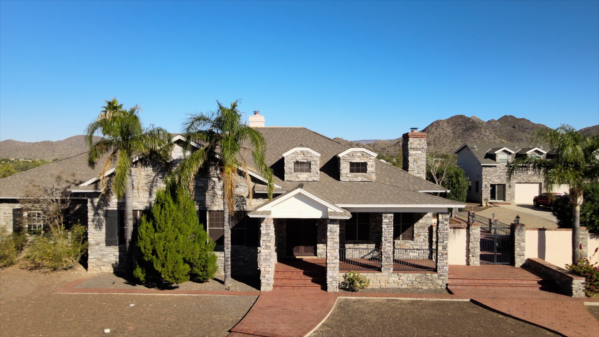 Stone residence with covered porch, palm trees, and mountains