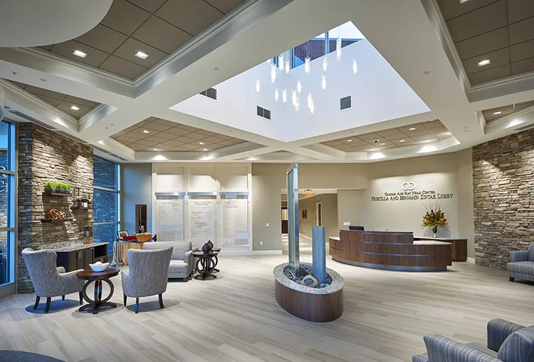 Spacious Caron reception lobby with stone accent walls, a curved front desk, skylight, lounge chairs, and modern decor