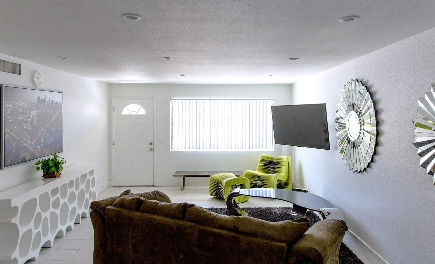 Modern living room with brown sofa, green lounge chair, wall-mounted TV, and decorative mirrors.