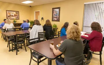 Group of people dining at shared tables in a bright, casual cafeteria at Arrowhead Behavioral Health in Maumee