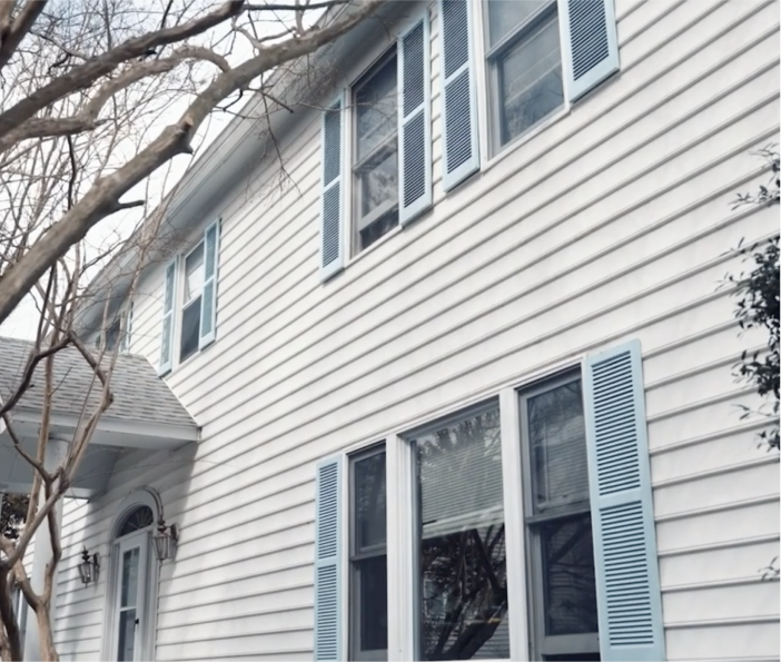 White two-story house with blue shutters and trees in front.