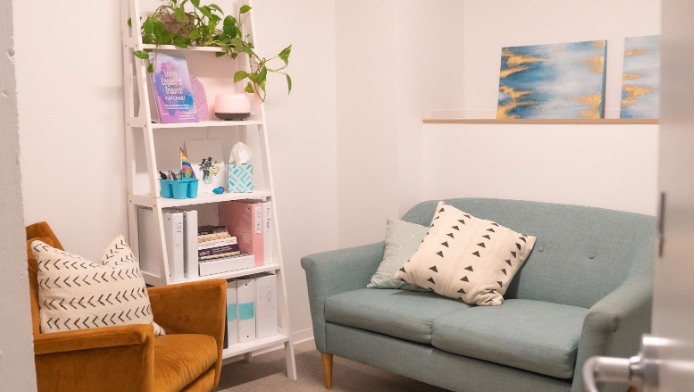 Cozy therapy room with sofas, pillows, shelving, and artwork