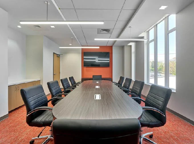 Meeting room with long table, black chairs, and mounted screen