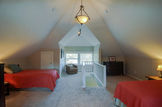 Carpeted loft bedroom with two beds, a reading chair by the window, and warm lighting