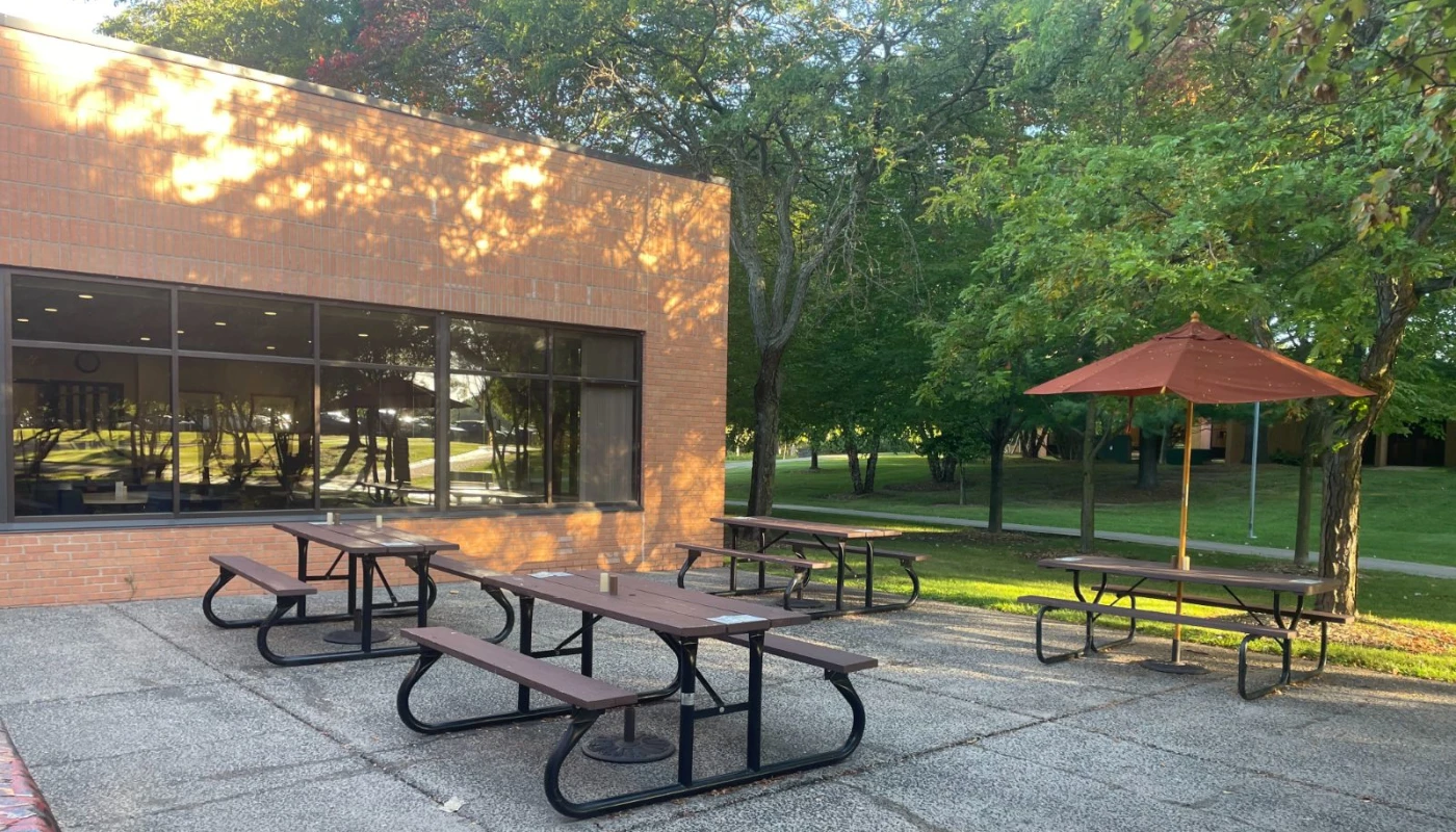 Picnic tables outside brick building under tree shade