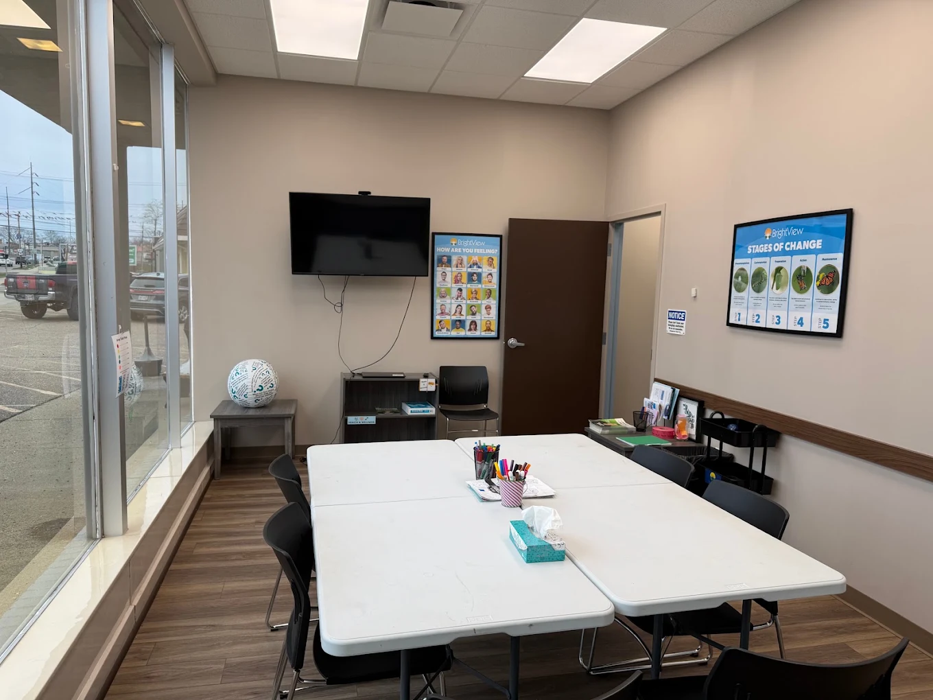 BrightView Health meeting room with tables and chairs, wall-mounted television, recovery education posters, and large front windows