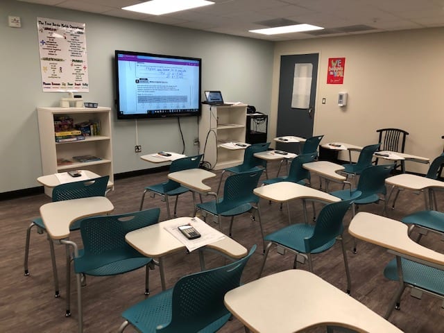Classroom with teal chairs, white desks, and smart board