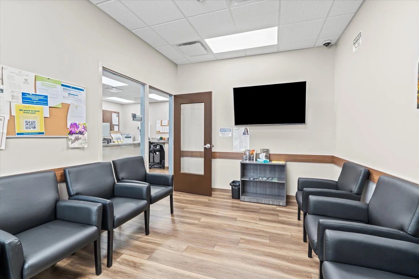 BrightView Health treatment waiting room with black armchairs, wall-mounted television, bulletin board, and wood-look flooring