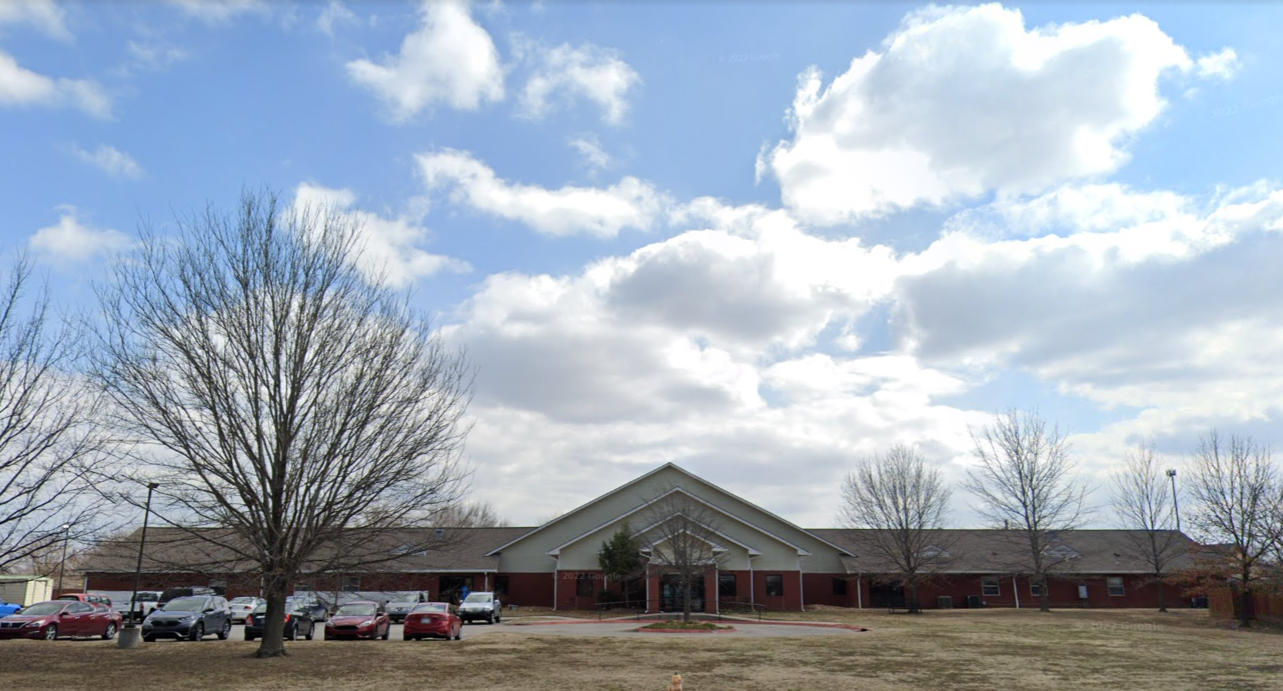 Front of facility featuring trees and parking by entrance.