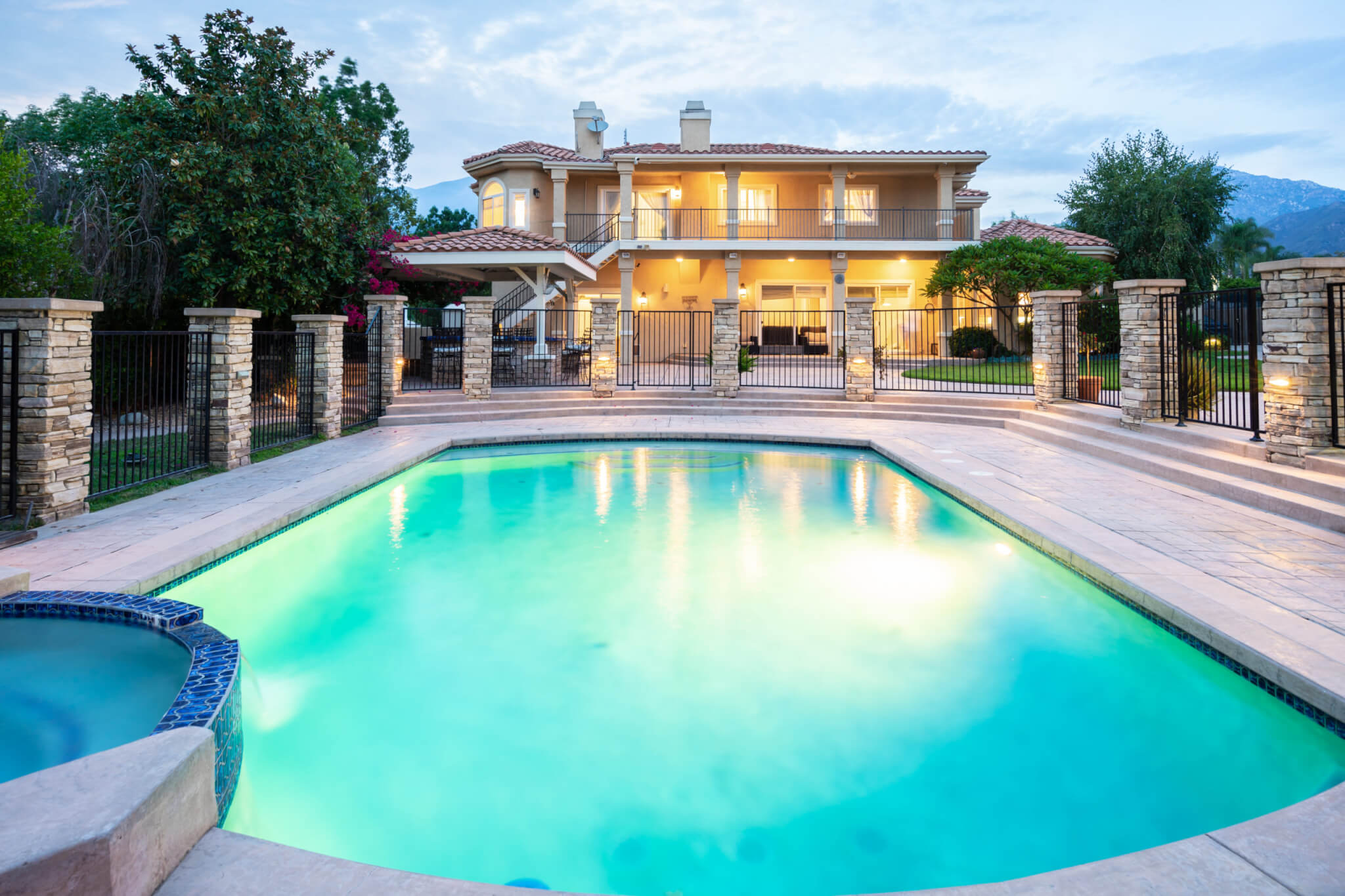 Large outdoor pool facing a two-story residence at dusk