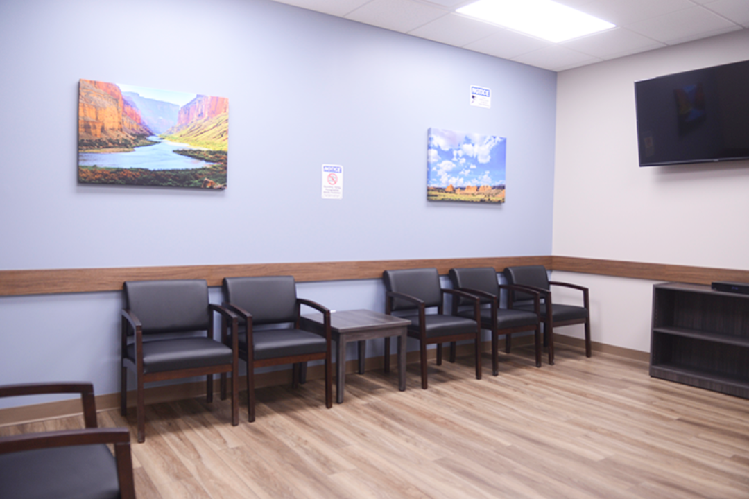 BrightView Health clinical room with patient chair, wheeled vital-sign monitor, blue accent wall, and wood-look flooring