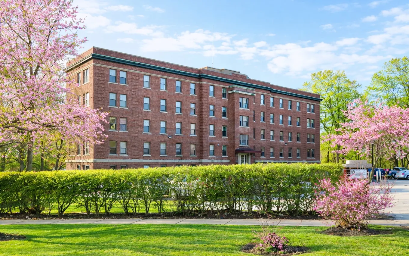 Brick residential facility surrounded by trees and flowering shrubs