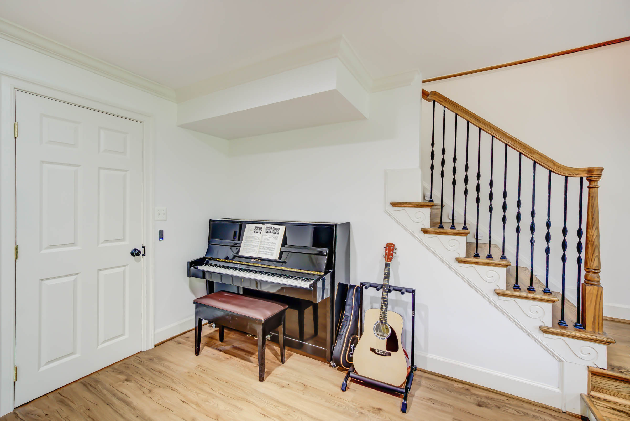 Upright piano and guitar beside staircase.
