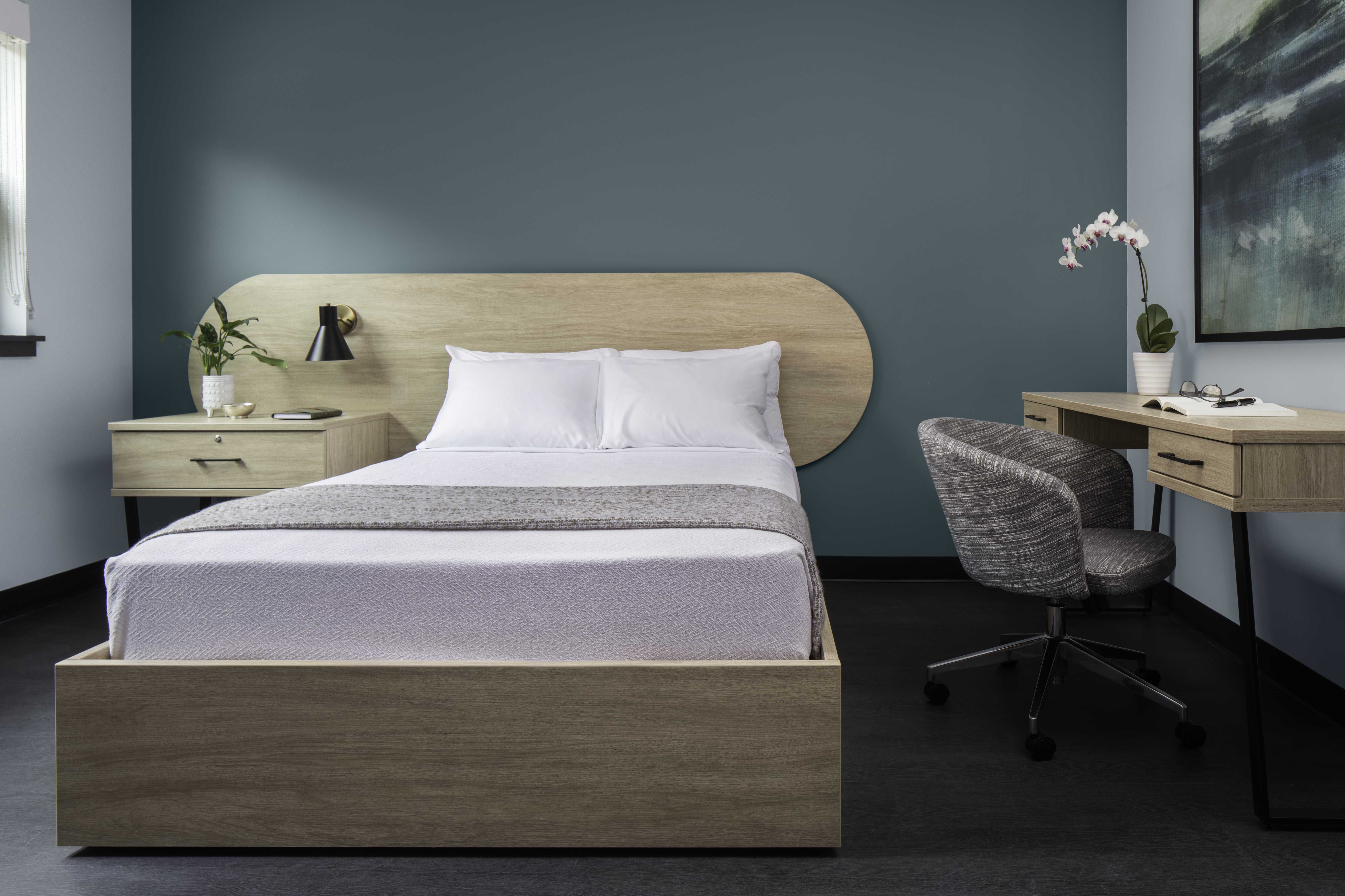 Bed with wood frame, teal wall, desk, and chair