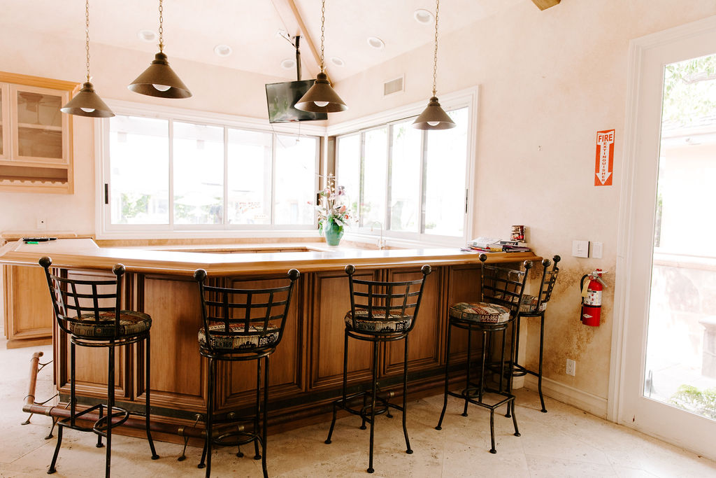 Bright room with wraparound wooden counter, bar stools, and large windows, decorated with pendant lights and a wall-mounted TV