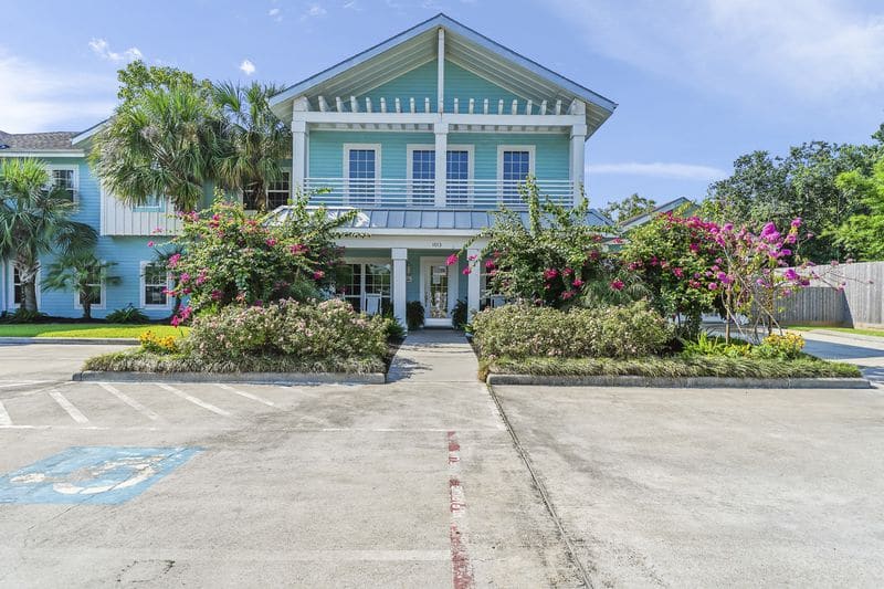 Exterior view of light blue two-story building with white trim and blooming landscaping