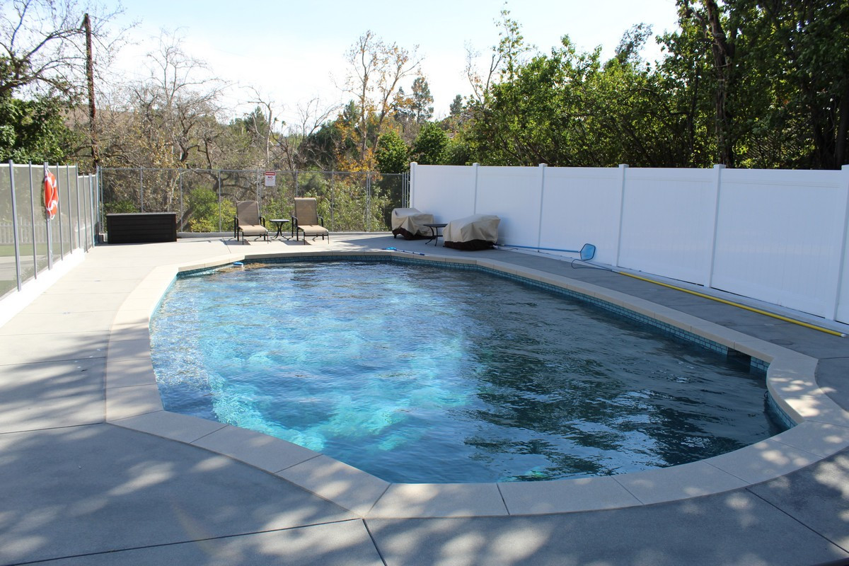 Outdoor swimming pool with lounge chairs and privacy fence