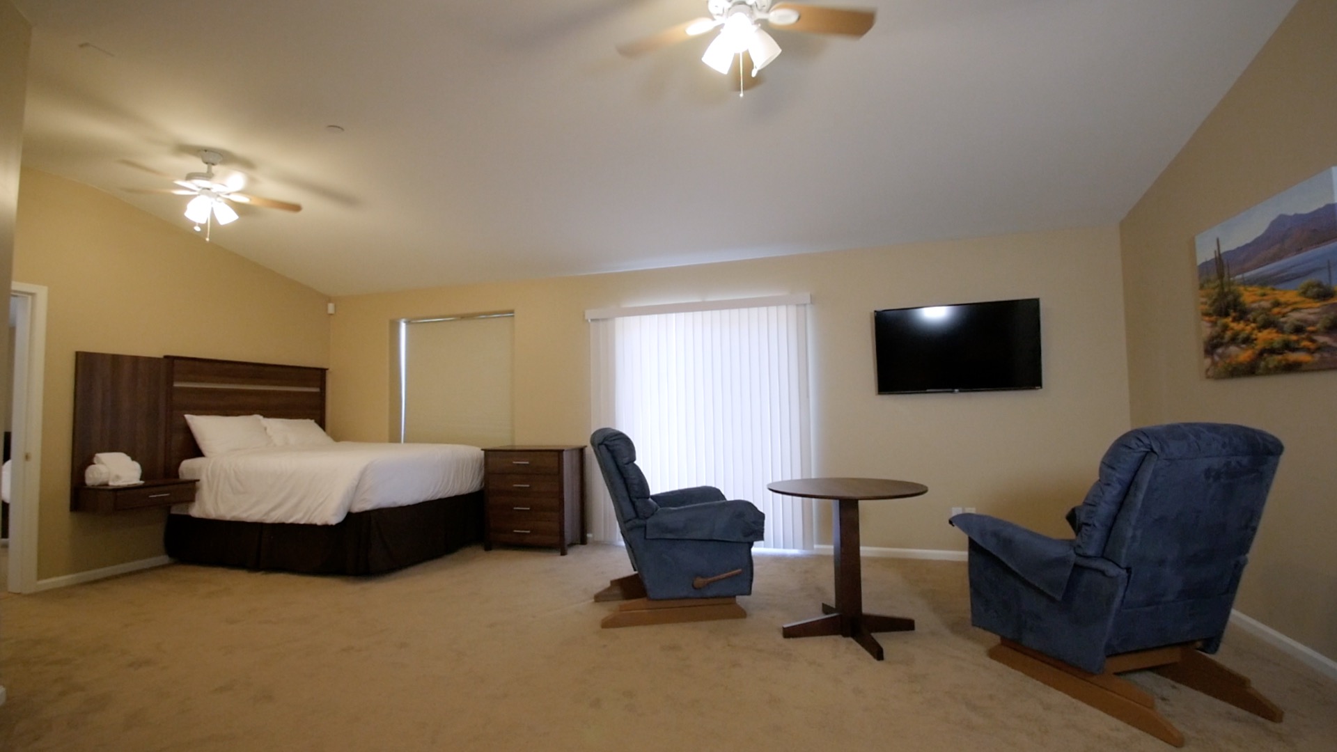 Spacious bedroom with bed, recliners, table, and television