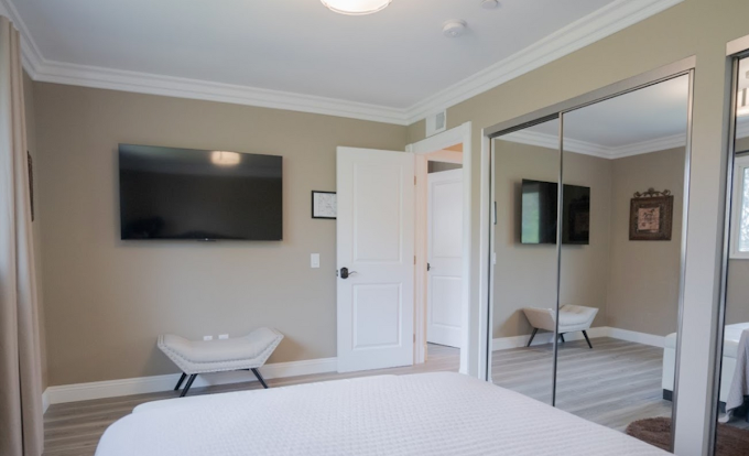 Bedroom with TV, mirrored closet, and neutral-toned decor