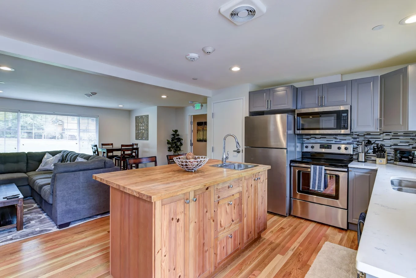 Open-concept kitchen with stainless steel appliances, wood island, and view into living and dining space with sectional sofa