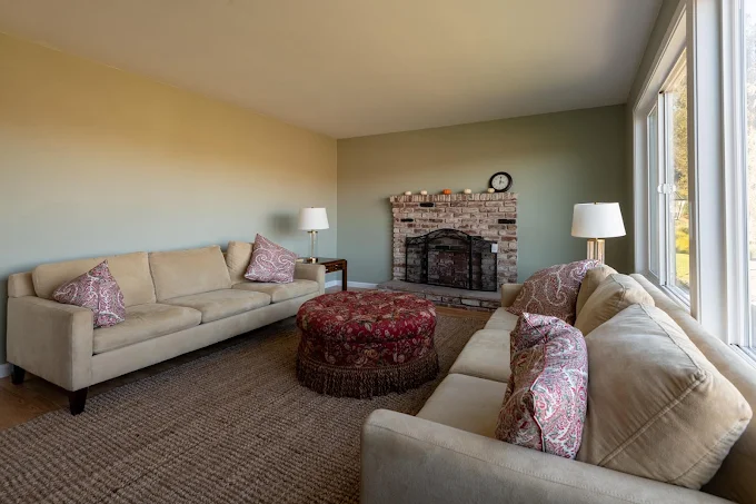 Two beige sofas with ottoman and brick fireplace