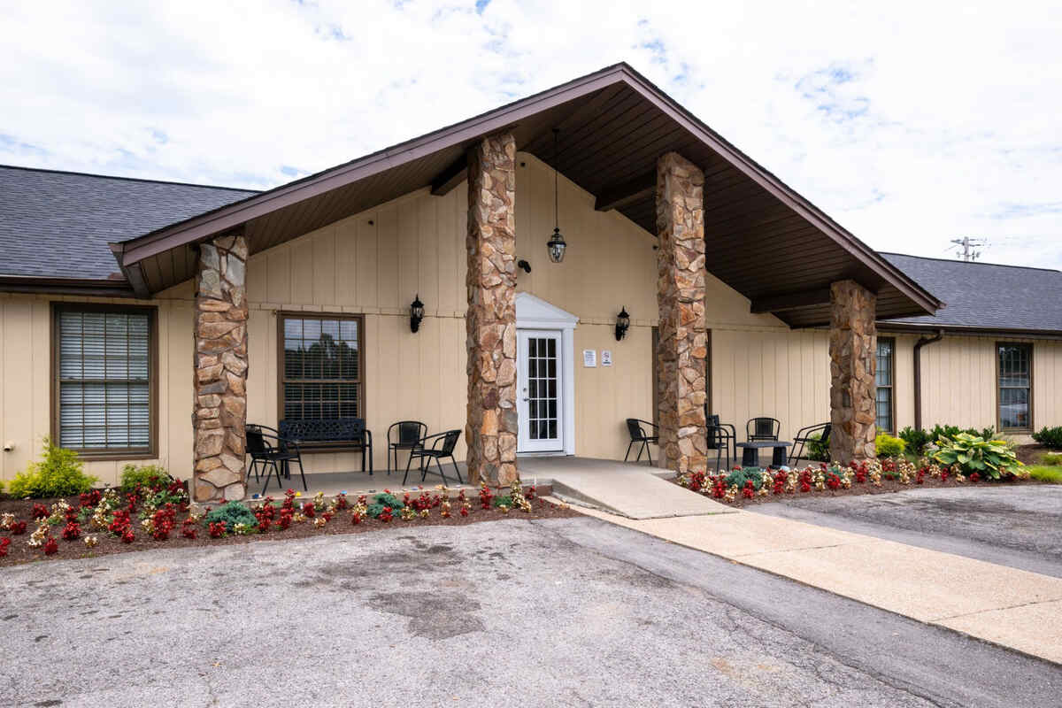 Rehab facility entrance with stone pillars, outdoor seating, and flowers.