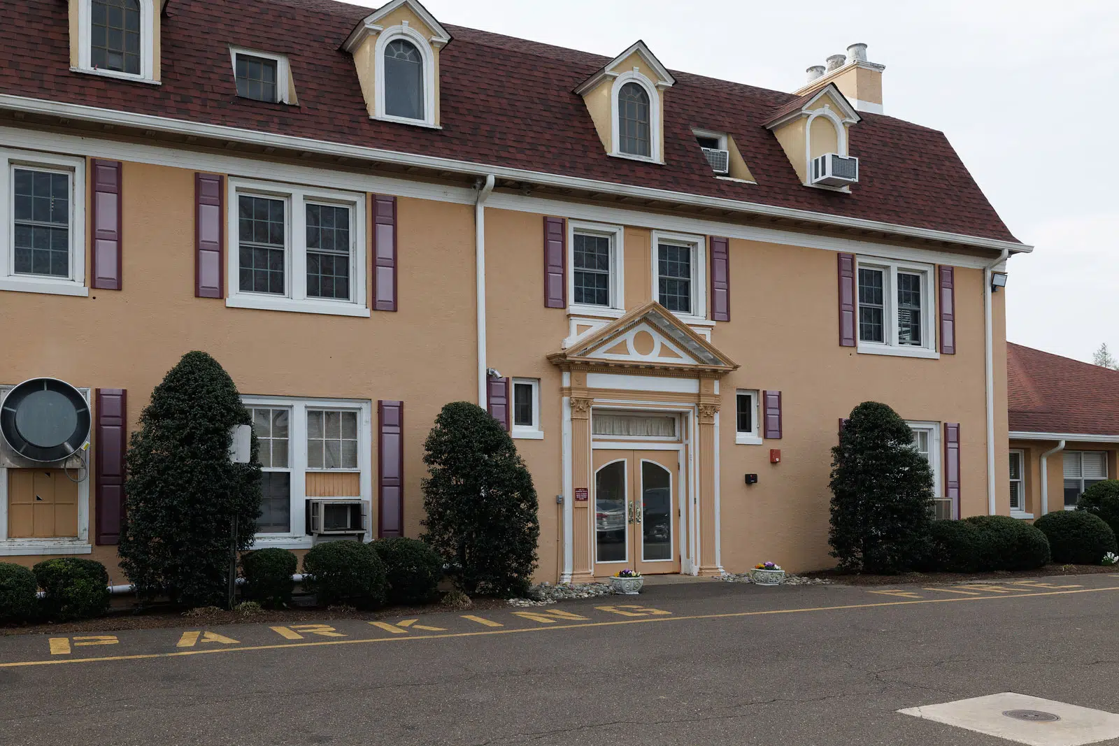 Close exterior view of entrance with windows and trimmed shrubs