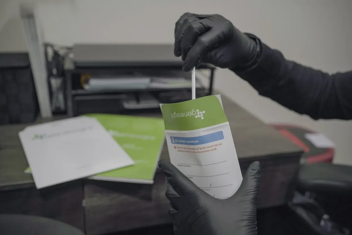 Gloved clinician placing a swab into a Genesight testing envelope.