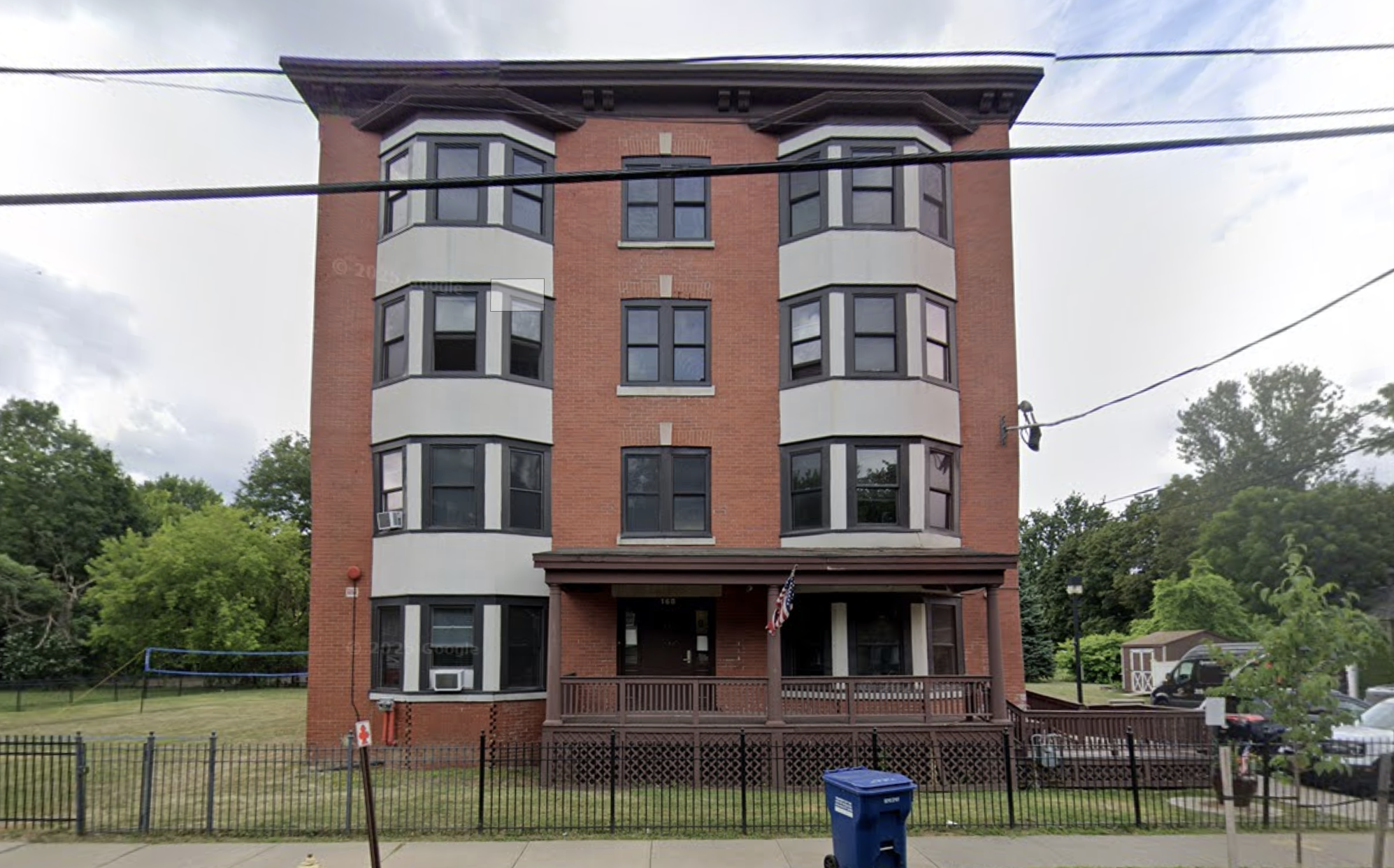 Four-story brick building with front porch and fenced lawn