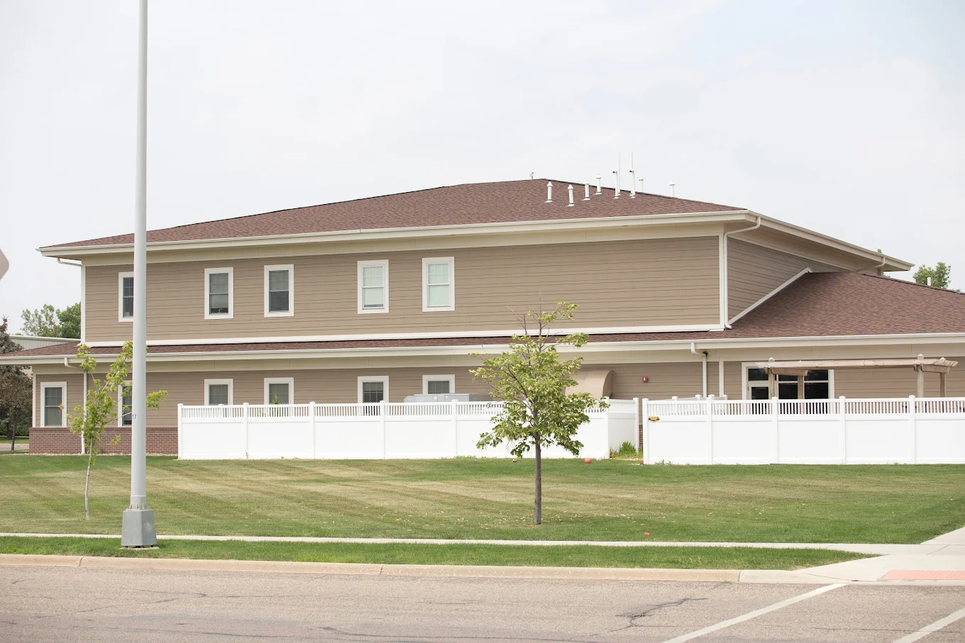 Two-story beige building with fenced yard and green lawn