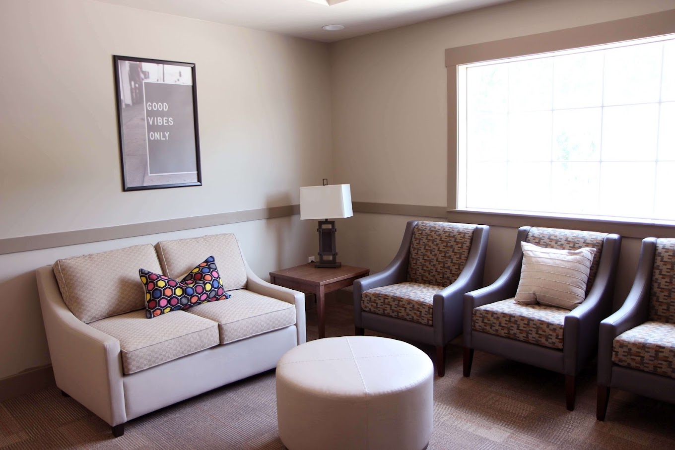 Cozy waiting room with a beige couch, gray chairs, and a "Good Vibes" sign.