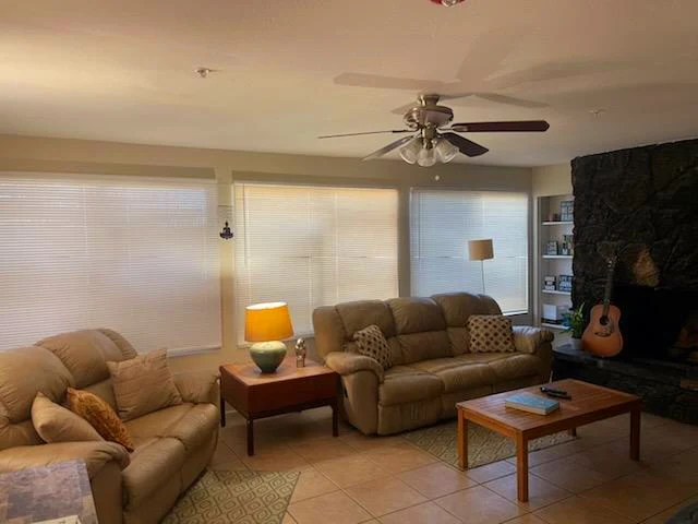 Cozy living room with beige sofas, a wooden coffee table, a stone fireplace, and large windows with blinds