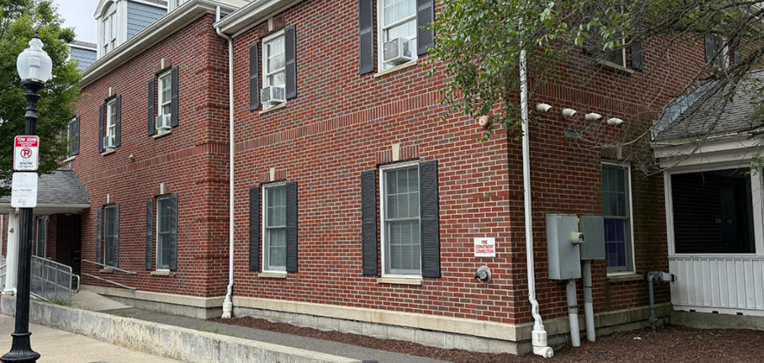 Brick building side entrance with black shutters and adjacent sidewalk