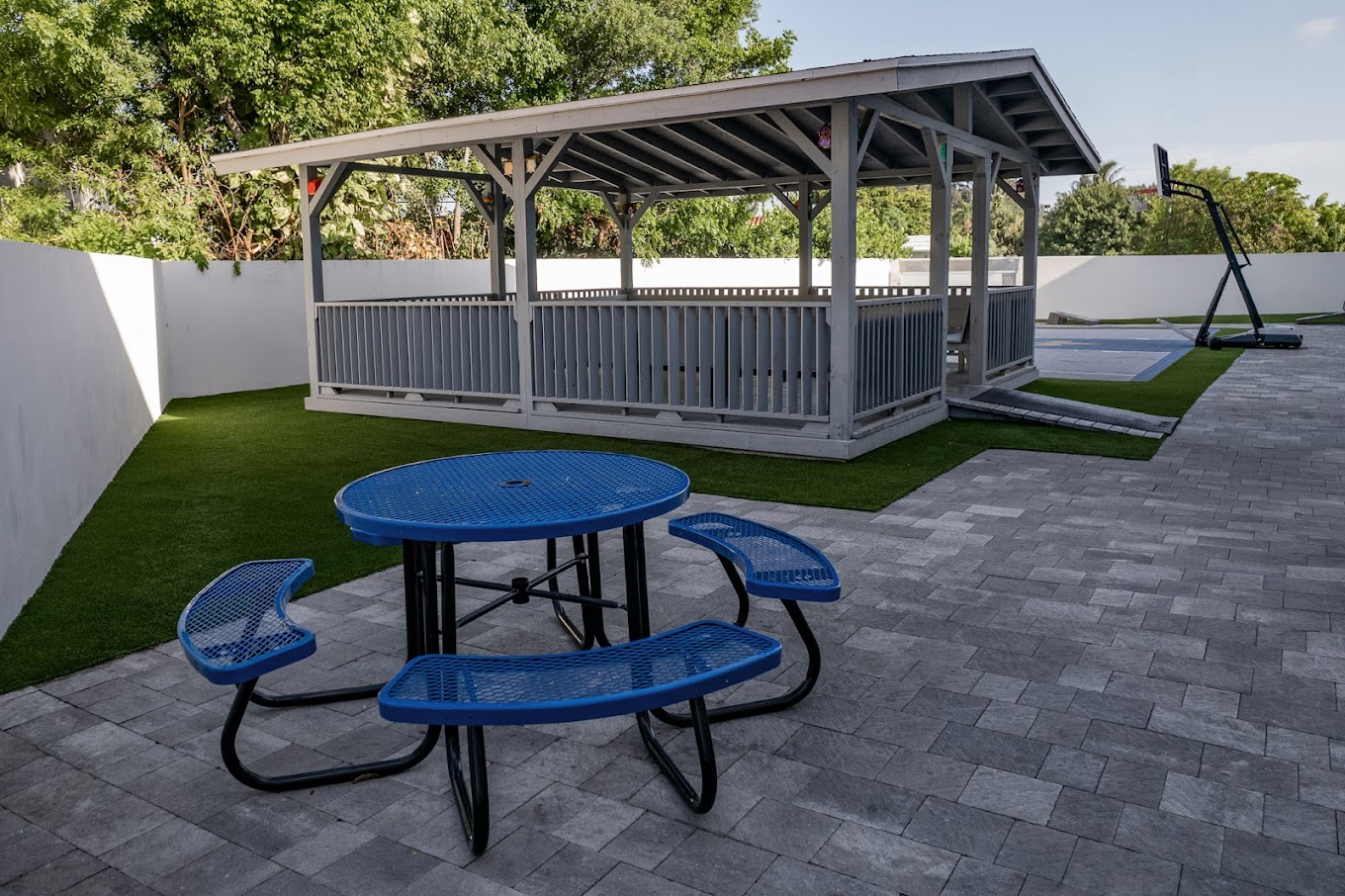Outdoor area with a gazebo, table, and a basketball court.