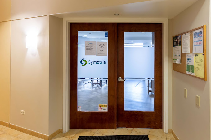 Glass double doors with a "Symetria" logo leading to a facility.