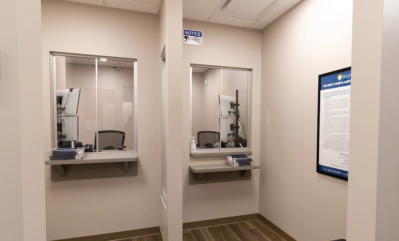 Two OTP dispensing service windows at BrightView Health with privacy partitions, counters, computer workstations, and patient information displayed on the wall