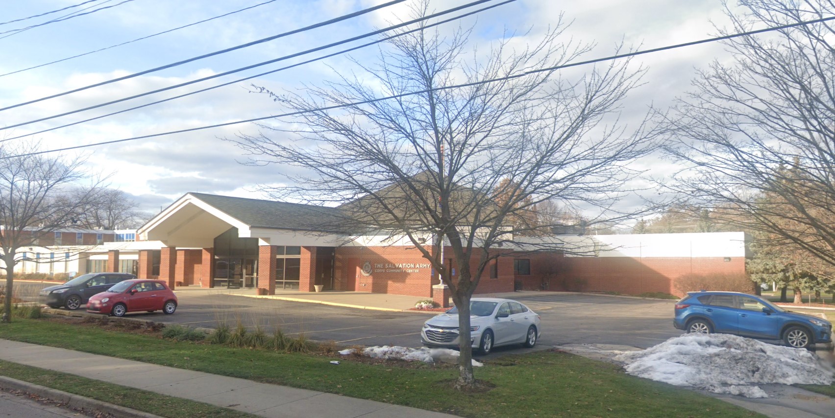 A brick building with a gable roof, seen from the parking lot, with a few cars parked in front.