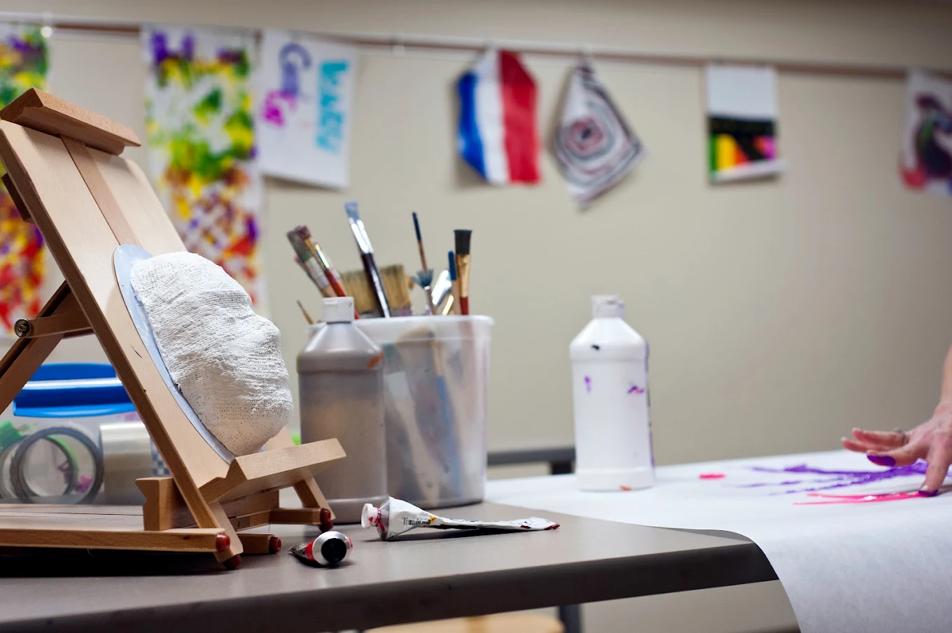 Art therapy workspace with easel, paintbrushes, paints, and artwork