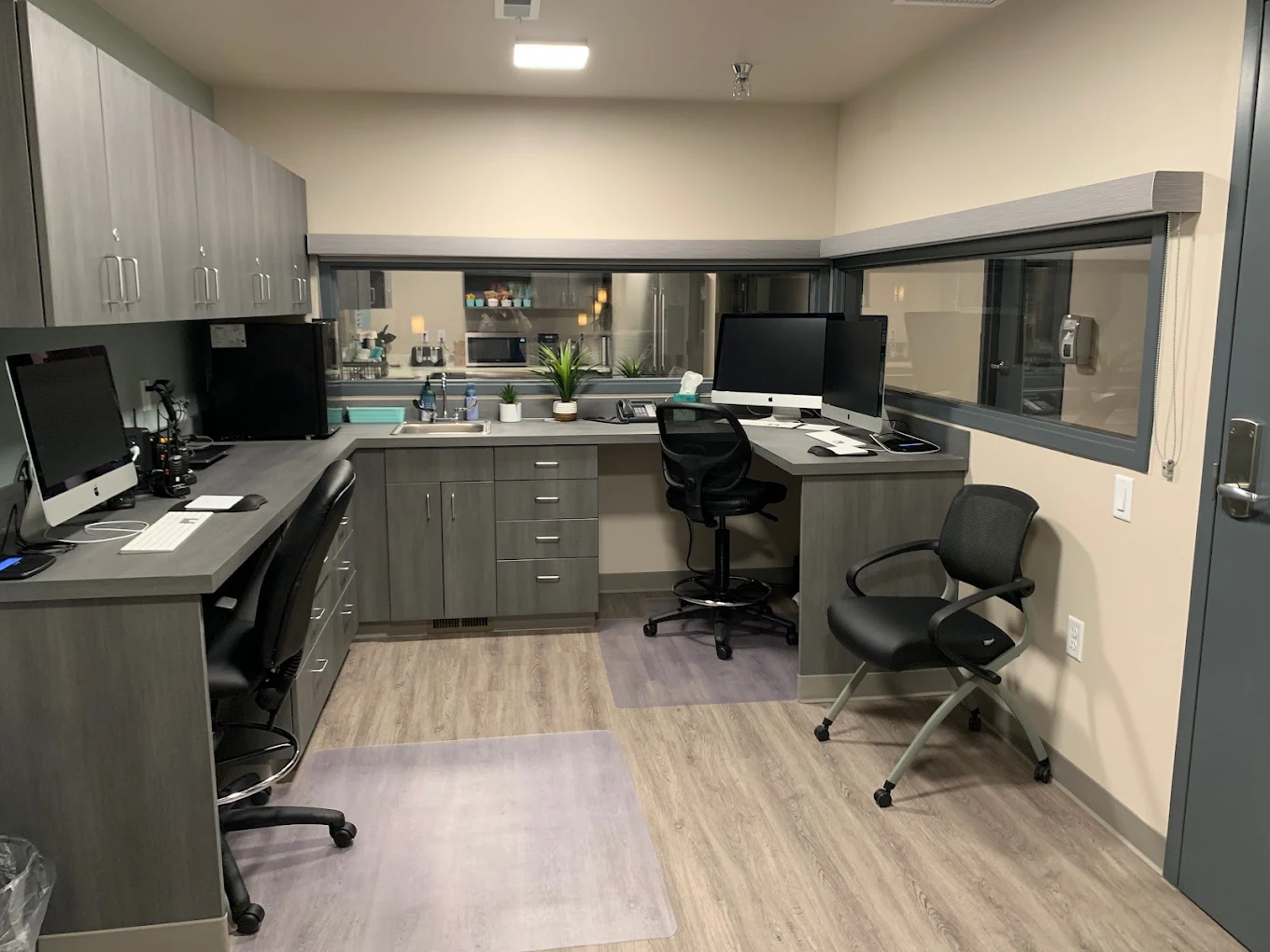 Staff office with workstations, desktop computers, overhead storage, and interior windows for visibility