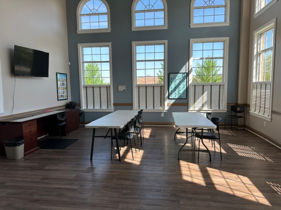 Bright group counseling room at BrightView Health with tables, chairs, television, wood flooring, and tall arched windows