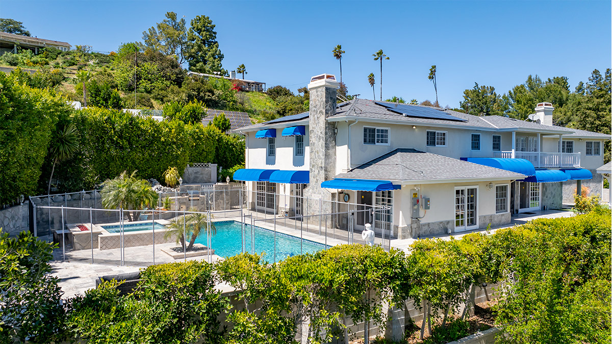 A rehab facility with a pool, blue awnings, and lush greenery.