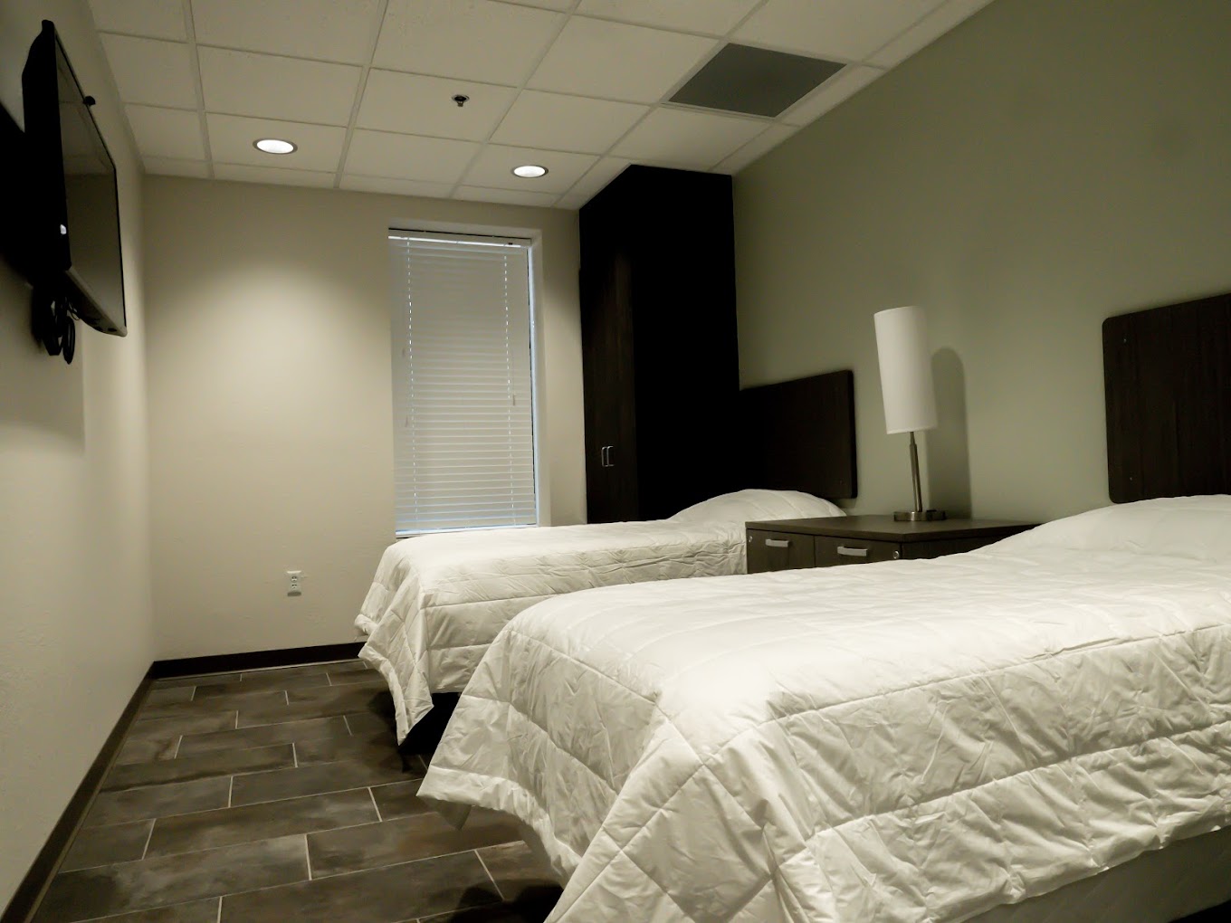 A modern rehab bedroom with two twin beds, a TV, and soft lighting.