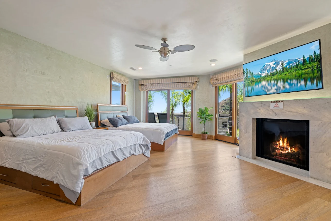 Large double bedroom with fireplace, two beds, wood flooring, and doors opening to a balcony with palm tree views