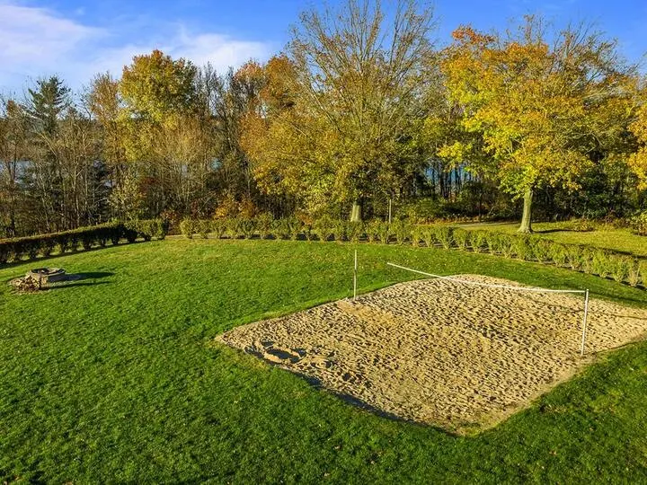 Grassy outdoor area with sand court surrounded by trees