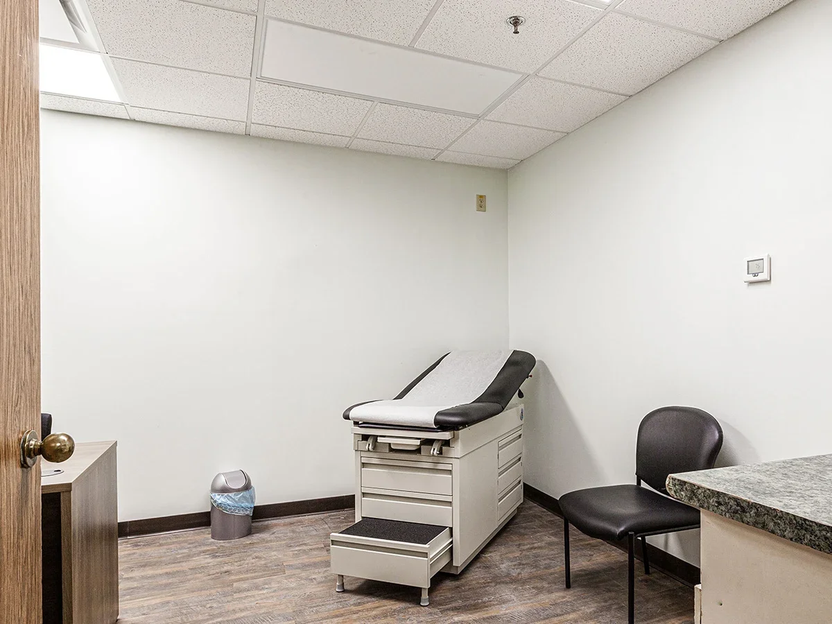 Exam room with medical bed, chair, and small trash bin