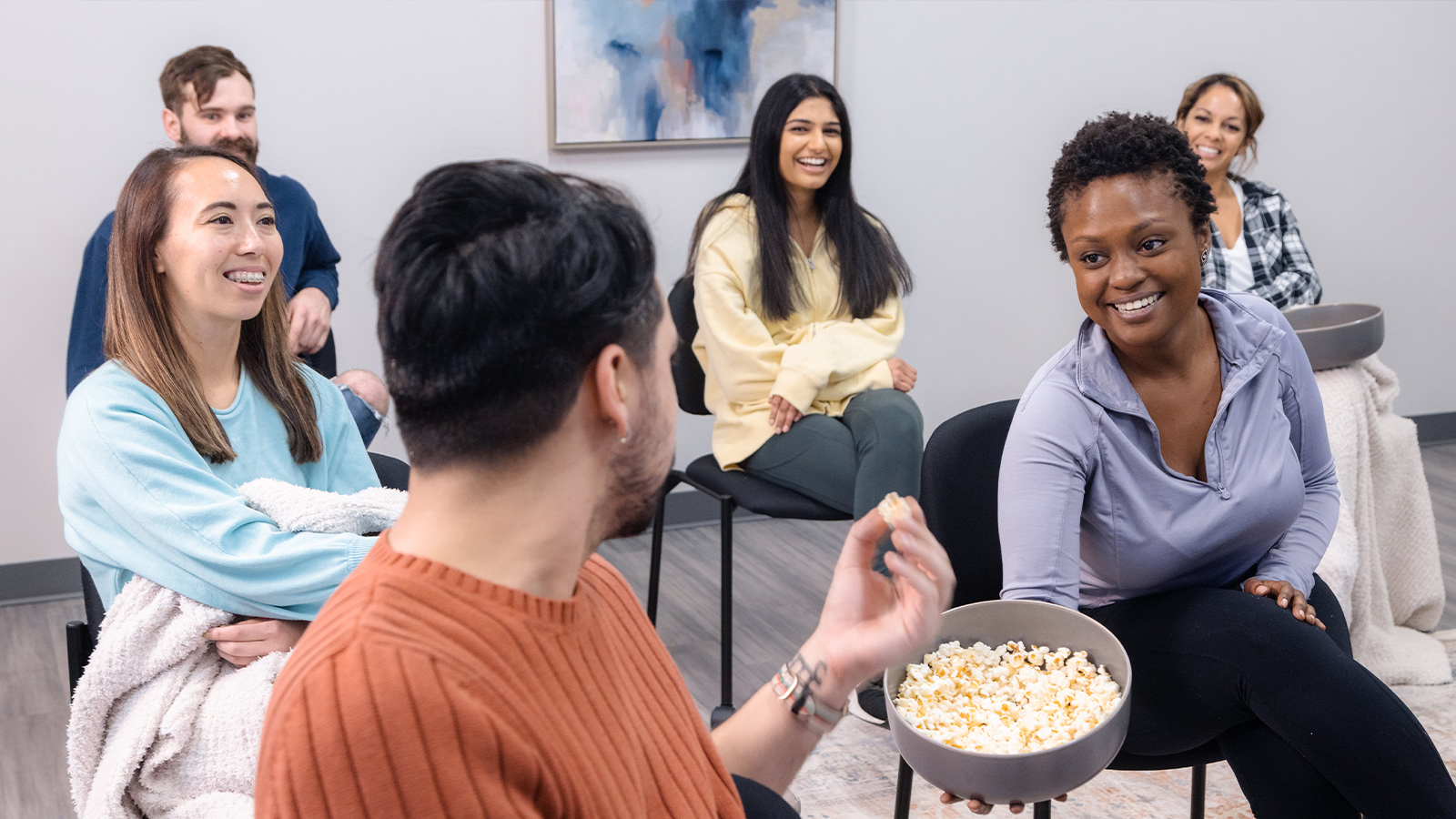 A group of people laughing while sharing snacks in a therapy session.