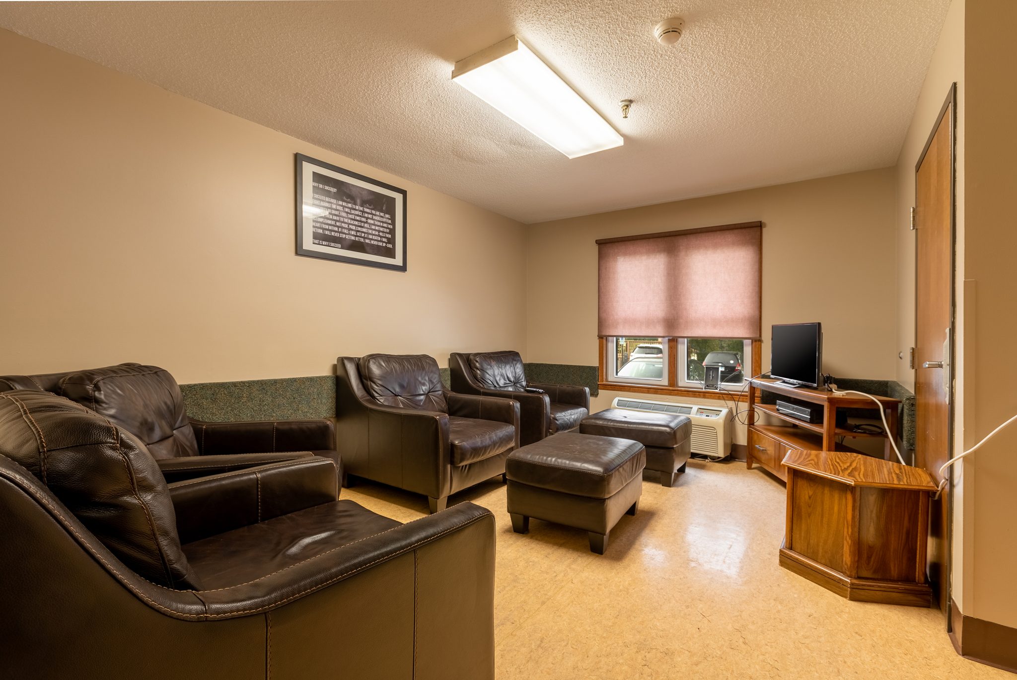 Cozy lounge with leather seating, ottomans, and a TV near a window.