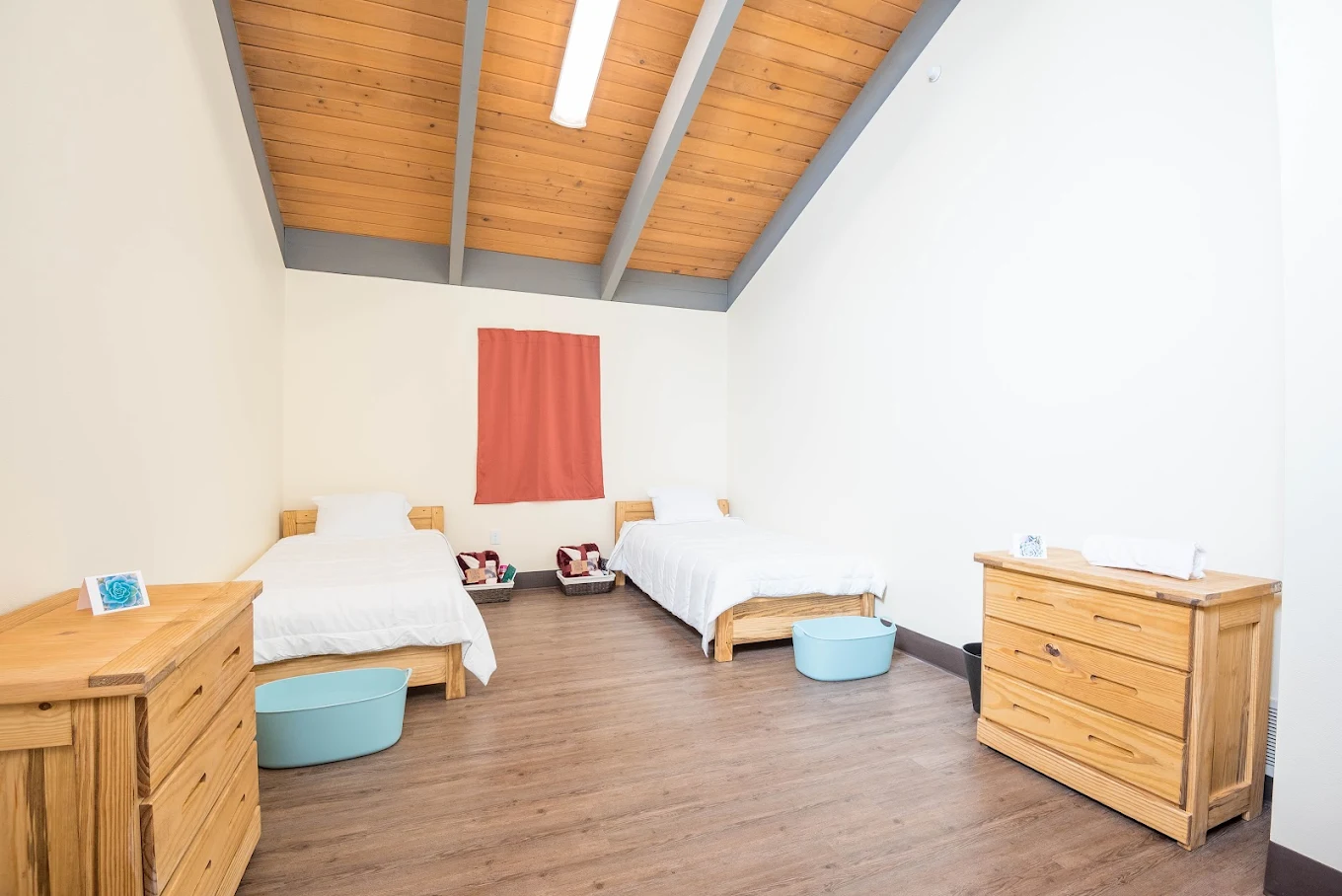 Minimalist double bedroom with wooden beds, white bedding, and exposed wood beam ceiling