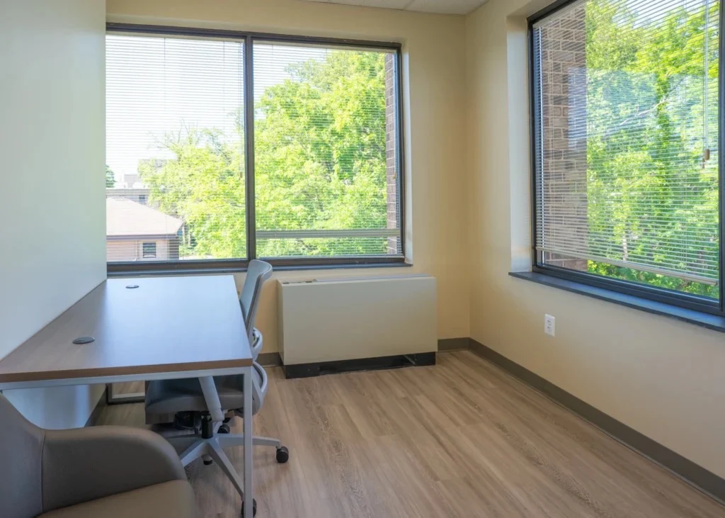 Private office with desk and large windows overlooking trees