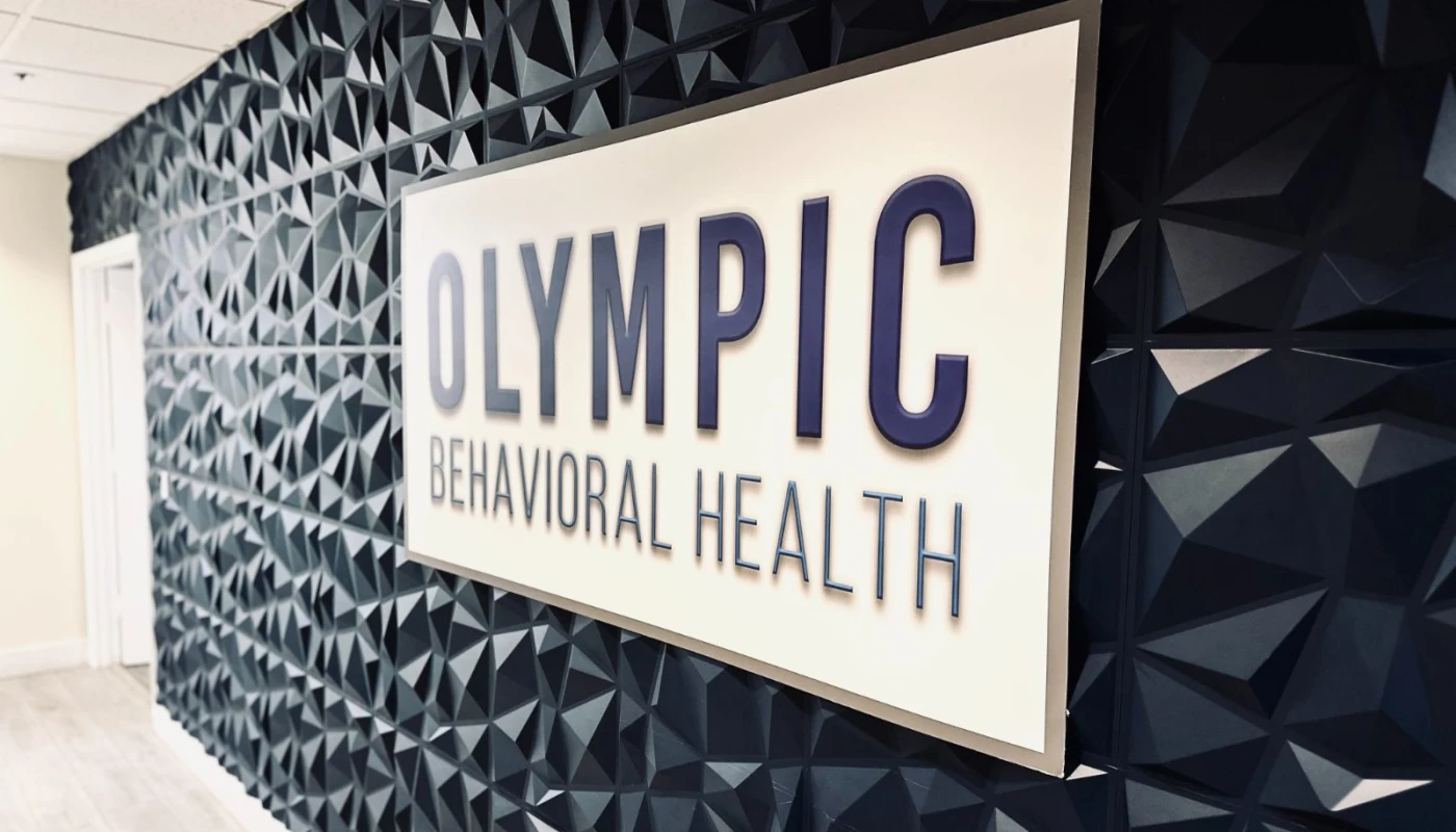 Close-up of Olympic Behavioral Health logo on a textured wall.